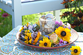 Glas mit Schneckenhäuschen  in Tellerkranz aus Blüten