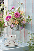 Strauß aus Rosen und Malven im alten Teekessel aufgehängt