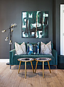 Turquoise velvet sofa with scatter cushions and small side tables below abstract painting on wall