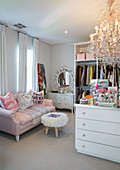 Pink sofa, fur-covered stool, dressing table and chandelier in feminine dressing room