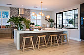 Wooden stools at long, glossy, white island counter in kitchen