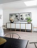 Houseplants and vases on sideboard below black-and-white pictures on wall