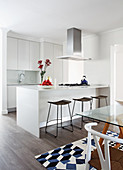 Island counter and bar stools in white, open-plan kitchen with glass table in dining area