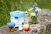 Kleiner Blumenstrauß, Lunchbag aus Wachstuch, Bügelflasche, Apfel, Ei und Tomaten im Glas beim Picknick