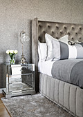 Grey bed with high headboard and mirrored bedside cabinet against grey wall