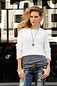 A young blonde woman wearing a t-shirt, a white jumper and jeans