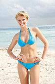 A blonde woman on a beach wearing a blue bikini