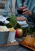 A Fall table with apples, popcorn, chips, apple cider with cinnamon and star anise, greenery and a woman holding a glass of red wine