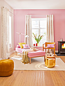 A day bed, a chair, a wood-burner, a golden side table and a pouffe in a living room painted in shades of pink