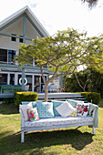 Colourful shabby-chic scatter cushions on bench in summer garden in front of house