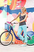 A blonde woman wearing a black-and-white polka dot top and light blue trousers with a bike