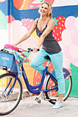 A blonde woman wearing a black-and-white polka dot top and light blue trousers with a bike