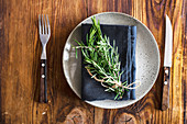 Rustic table setting with ceramic plate decorated with napkin and rosemary