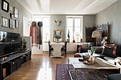 Coffee table, sofa and TV cabinet in front of dining area, armchair and screen in open-plan interior