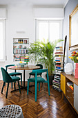 Various petrol-blue chairs around dining table below window