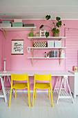 Yellow chairs at desk below shelves on pink wall