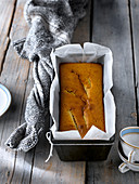 Baked golden pear cake in metal form with parchment on rustic gray table