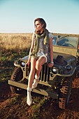 A brunette woman wearing a scarf, t-shirt and shorts sitting on a jeep