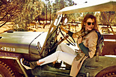 Brünette Frau in Safari-Look sitzt im Jeep, im Hintergrund Zebras