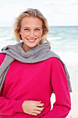 A young blonde woman wearing a pink jumper with a grey jumper over her shoulders