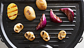 Potatoes, red onions and mushrooms on a grill