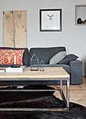 Grey couch against wooden panel on wall behind candles and metal house-shaped ornaments on coffee table in living room