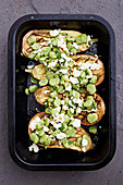 Broad beans sprinkled over aubergines with cheese in a roasting dish