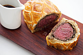 Sliced Beef Wellington on a wooden board with a jus