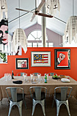 Glasses and candle lanterns on dining table, classic chairs, retro posters on orange partition and pendant lamps