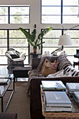 View past books on table to vintage leather sofa with fur blanket and cushions, armchair and houseplant
