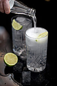 Tonic being poured into a Gin and Tonic with lime wedges