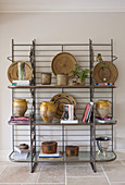 Collection of ceramics, raffia dishes and books on metal shelves