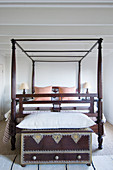 Oriental trunk with large cushion on top at foot of wooden four-poster bed