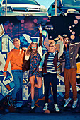 A group of young people wearing fashionable clothing jumping in front of a graffitied wall