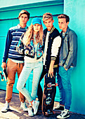 A group of young people wearing fashionable clothing posing against a wall with skateboards