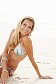 Reife blonde Frau im Bikini sitzt im Sand am Strand