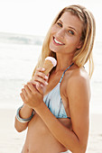 Blonde Frau mit Eis im Bikini am Strand