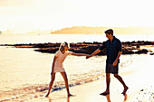 A young couple holding hands on a beach at sunset