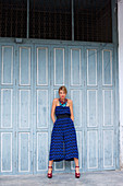 A young woman wearing a sleeveless, blue cropped jumpsuit and red high heels