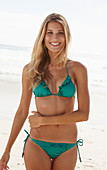 A blonde woman on a beach wearing a turquoise bikini