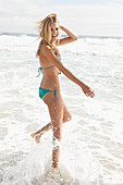 A blonde woman on a beach wearing a turquoise bikini