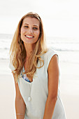 A mature blonde woman on a beach wearing a long top
