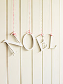 Die Buchstaben 'Noel' als Schriftzug aufgehängt vor weisser Holzwand