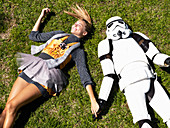 A young woman wearing a dress lying on a lawn with a Stormtrooper