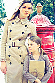 A young woman wearing a beige coat and a little girl with a package standing next to an old-fashioned British postbox