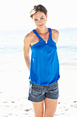 Reife brünette Frau mit blauem Top und silbernem Armband am Strand