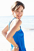 A mature brunette woman on a beach wearing a blue top