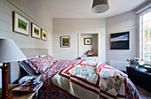 Patchwork bedspread on gray upholstered bed in bedroom with white wooden walls