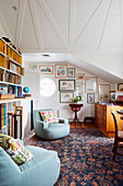 Two light blue armchairs next to bookcase in room under sloping ceilings