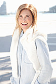 A blonde woman wearing a denim shirt with a white knitted jumper over her shoulders